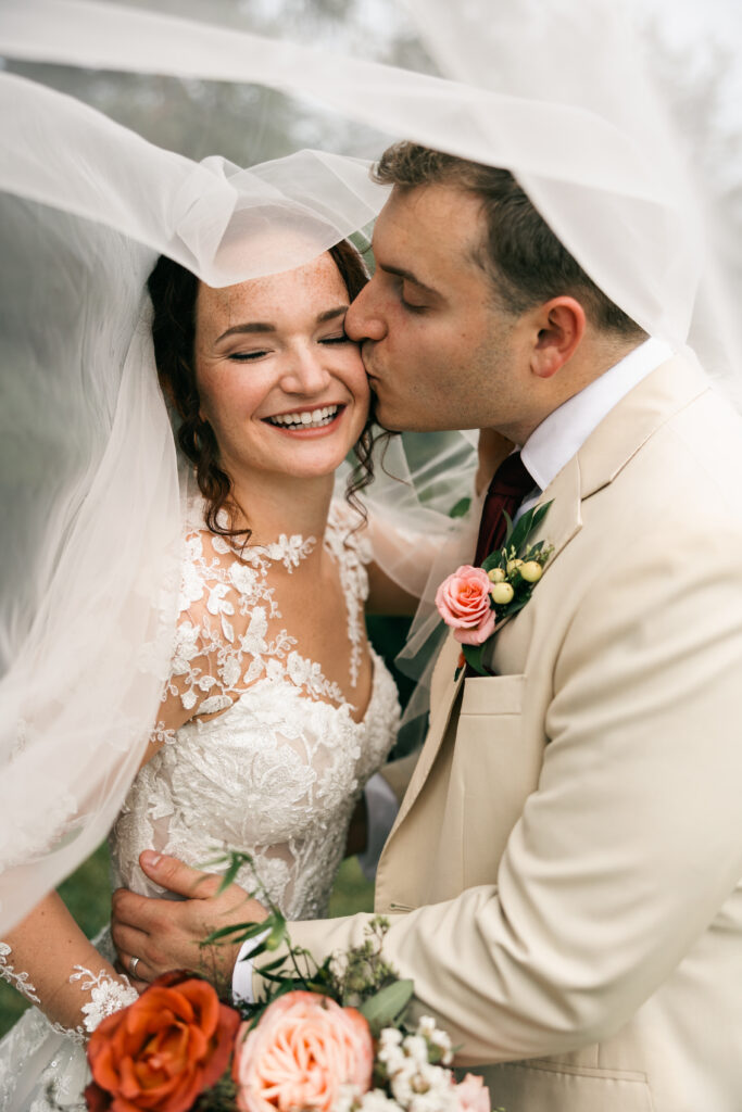 groom kissing bride's cheek under veil